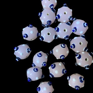 May include: A collection of pink glass beads with blue and white evil eye designs. The beads are round and have a hole in the center for stringing.