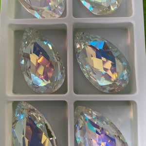 May include: Six iridescent teardrop-shaped crystal pendants in a white plastic storage box. The crystals are clear with a rainbow sheen.