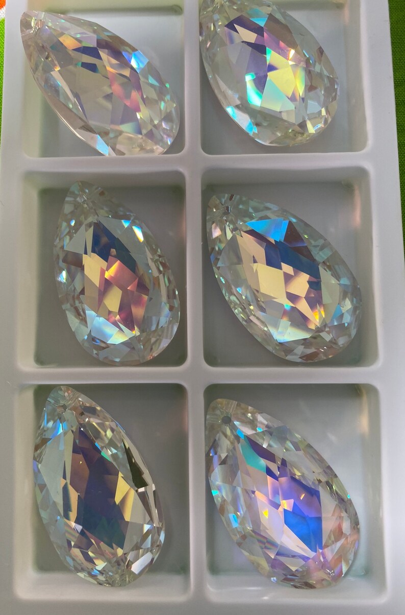 May include: Six iridescent teardrop-shaped crystal pendants in a white plastic storage box. The crystals are clear with a rainbow sheen.