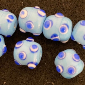 May include: A collection of six blue glass beads with white and blue polka dots. The beads are all the same size and shape, and they are arranged in a random pattern.