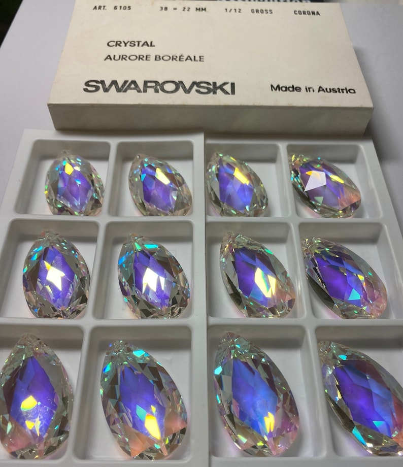 May include: Twelve iridescent crystal teardrop pendants in a white box. The box is labeled "Swarovski" and "Made in Austria".
