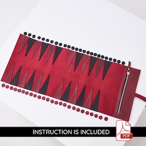 May include: A red leather backgammon set with black and red triangles. The set is rolled up and has a zipper closure. The set comes with black and red playing pieces.