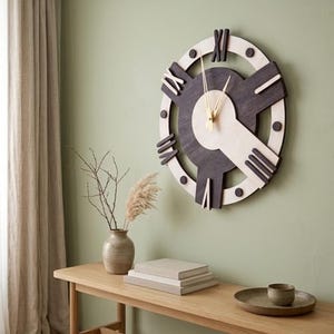 May include: A circular wall clock featuring a two-tone design with dark charcoal and light natural wood elements. The clock face displays large Roman numerals and thin gold-coloured hands, creating a geometric aesthetic with layered wood segments.