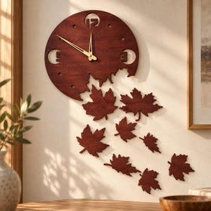 May include: A circular dark wood wall clock featuring a cutout design of falling maple leaves. The clock face displays gold-colored hour and minute hands, with the number 12, 3, 6, and 9 represented by cutouts and circular markers.