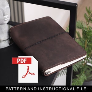 May include: A brown leather notebook cover with a black elastic closure. The cover is lying on a black surface with a white background. The text "PDF" is in red on a white background with a red Adobe Acrobat logo. The text "PATTERN AND INSTRUCTIONAL FILE" is below the logo.