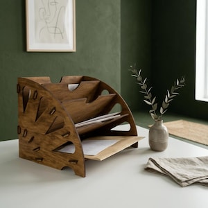 Op de afbeelding: Een donkerbruine houten bureau-organizer met drie trapsgewijze vakken voor documenten en papieren. De zijpanelen zijn voorzien van een decoratief uitgesneden patroon. De organizer is gemaakt van hout met een zichtbare houtnerf.