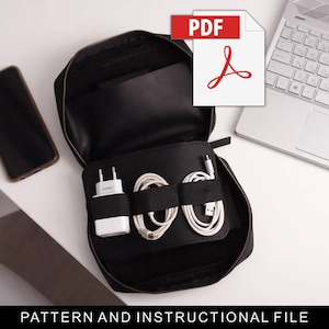 May include: A black zippered pouch with multiple compartments for organizing electronics. The pouch is open and contains a white phone charger, two white cords, and a black phone. The pouch is on a white surface next to a silver laptop.