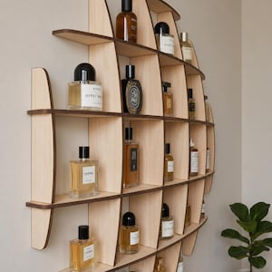 May include: A wall-mounted light wood shelving unit with a curved, organic shape featuring multiple compartments. The shelves are filled with various glass perfume bottles of different shapes and sizes, containing liquids in shades of amber and clear.