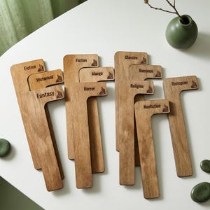 May include: A set of L-shaped wooden shelf dividers with laser-engraved text labels including Fiction, Historical, Fantasy, Manga, Horror, Classics, Romance, Religion, Nonfiction, and Dystopian, each featuring a small book icon graphic.