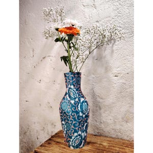 Peut inclure: Un vase en céramique bleu et blanc avec un motif floral. Le vase est rempli de fleurs blanches et orange.