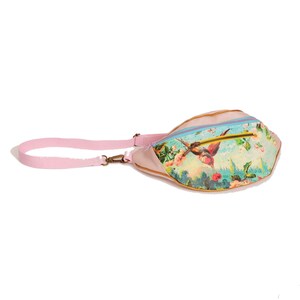 May include: A pink fanny pack with a floral print featuring a hummingbird. The bag has a gold zipper and a pink adjustable strap.