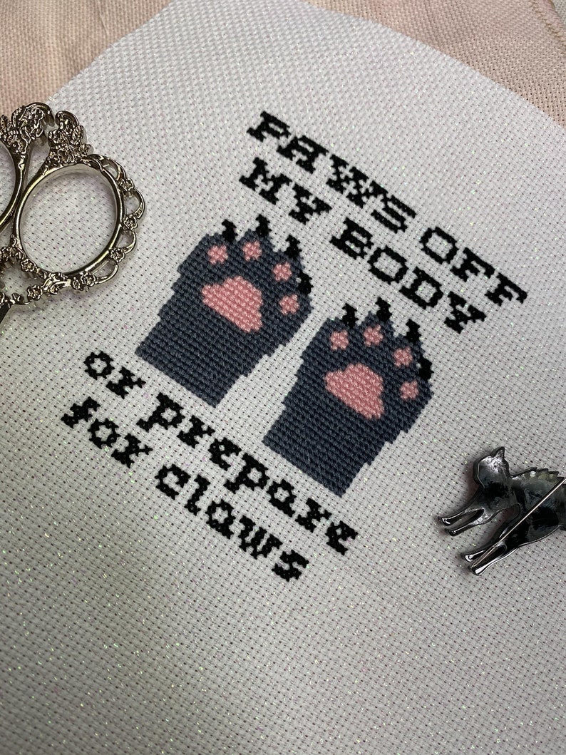 Puede incluir: Bordado blanco de punto de cruz con huellas de patas negras y rosas y el texto "PAWS OFF MY BODY or prepare for claws".