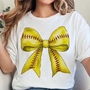 Könnte beinhalten: Ein weißes T-Shirt mit einer gelben Softball-Schleife mit roten Nähten. Die Schleife ist zu einem Knoten gebunden und die Enden schweben.