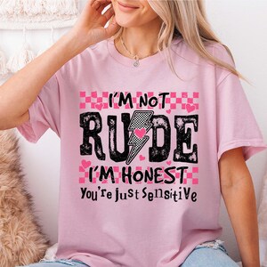 May include: Pink t-shirt with a graphic print that says "I'm not rude I'm honest you're just sensitive" with a lightning bolt and hearts.