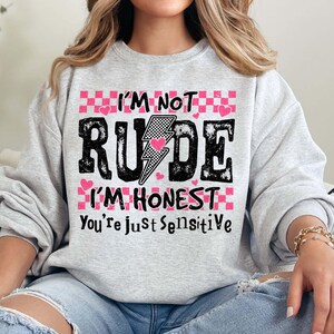 May include: A gray sweatshirt with a pink and black checkered pattern. The text on the shirt reads "I'm not rude I'm honest you're just sensitive".
