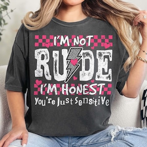 May include: A black t-shirt with a pink and white graphic that says "I'm not rude I'm honest you're just sensitive". The graphic includes a lightning bolt with a pink heart inside and a checkered pattern.