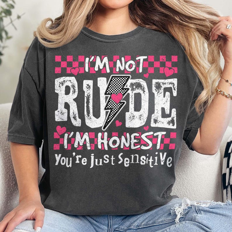 May include: A black t-shirt with a pink and white graphic that says "I'm not rude I'm honest you're just sensitive". The graphic includes a lightning bolt with a pink heart inside and a checkered pattern.