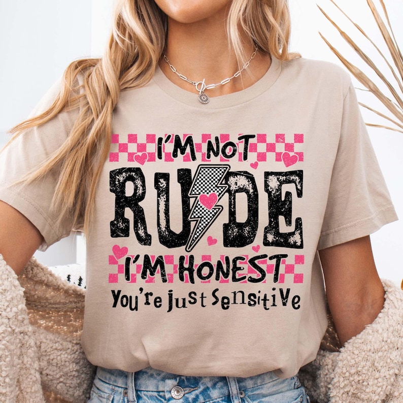 May include: A beige t-shirt with a black and white checkered pattern and pink hearts. The text on the shirt reads "I'm not rude I'm honest you're just sensitive".