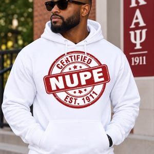 Può includere: Una felpa con cappuccio bianca caratterizzata da una grafica circolare rossa sul petto. La grafica include il testo "CERTIFIED NUPE" e "EST. 1911" all'interno di un design a timbro con stelle. La felpa ha maniche lunghe, una tasca a marsupio e lacci.