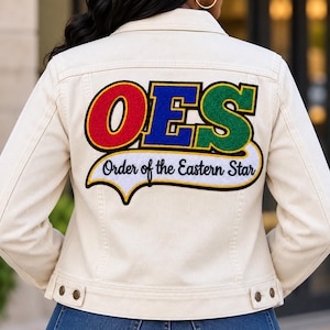 May include: An off-white denim jacket featuring a large back patch with the letters OES in red, blue, and green. Below the letters, a white banner with a black border displays the text Order of the Eastern Star in black script.