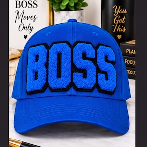 May include: A bright blue baseball cap featuring the word BOSS in large, textured, blue chenille letters with a black border. The cap has a structured crown, a curved brim, and stitched eyelets on the top panels for ventilation and a classic look.