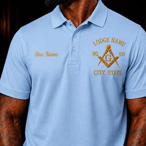 May include: A light blue polo shirt featuring a collar and three buttons. The chest displays gold embroidery with the text Bro Name on the right, and Lodge Name, No. 00, City, State, and a square and compass symbol with a G on the left.