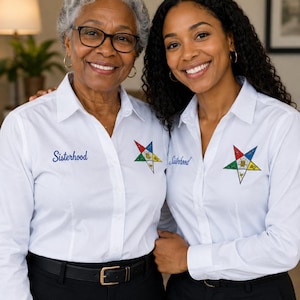 May include: Two white long-sleeved button-down shirts featuring the word Sisterhood embroidered in blue on the right chest and a multi-coloured five-pointed star emblem on the left chest, paired with black trousers and black belts.