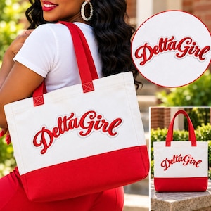 May include: A white canvas tote bag with a red bottom panel and red fabric handles. The front of the bag features the text Delta Girl embroidered in red script lettering with a white outline, matching the design shown in the circular inset.