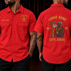 May include: A red short-sleeved button-down shirt featuring two chest pockets. The front displays 'Bro Name' and 'LODGE NAME CITY, STATE' with a square and compass emblem. The back features 'LODGE NAME', 'GOAT RIDER', 'NO. 00', and 'CITY, STATE' with a goat graphic.
