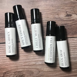 May include: Five small black roller bottles with white labels. The labels have the names of essential oil blends: Rose Garden, Spicy Ginger, Chilly Mojito, Afternoon Tea, and Bugs Away.