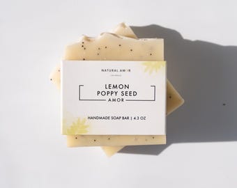 May include: Two bars of handmade lemon poppy seed soap, labeled "Natural Amor" and "Lemon Poppy Seed Amor", with a floral design and the text "Handmade Soap Bar | 4.3 oz".