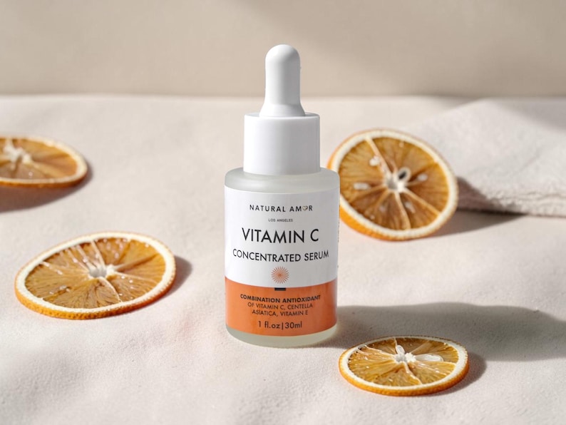 May include: A clear glass bottle of Vitamin C Concentrated Serum with a white dropper and orange label. The label reads "NATURAL AMOR" and "1 fl.oz/30ml". Dried orange slices are scattered around the bottle.