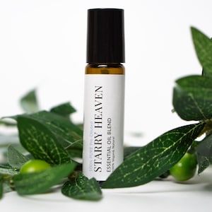 May include: A small glass bottle with a black cap and a white label that reads "STARRY HEAVEN 100% PURE Pre-Diluted ESSENTIAL OIL BLEND 100% Vegans Natural". The bottle is sitting on a white surface with green leaves.