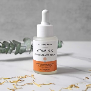 May include: A clear glass bottle of Vitamin C Concentrated Serum with a white dropper. The label includes the text "NATURAL AMOR" and "VITAMIN C CONCENTRATED SERUM". The bottom label is orange and lists ingredients. The bottle contains 1 fl oz (30ml).