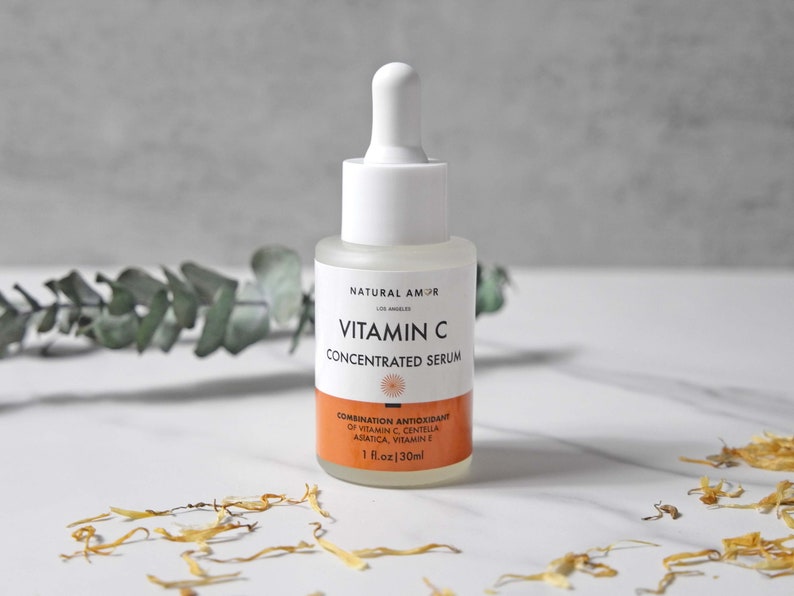 May include: A clear glass bottle of Vitamin C Concentrated Serum with a white dropper. The label includes the text "NATURAL AMOR" and "VITAMIN C CONCENTRATED SERUM". The bottom label is orange and lists ingredients. The bottle contains 1 fl oz (30ml).
