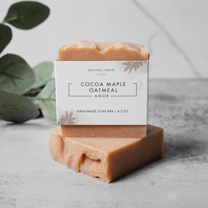May include: A bar of handmade soap with a white label that reads "Natural Amor Los Angeles Cocoa Maple Oatmeal Amor Handmade Soap Bar | 4.3 oz".