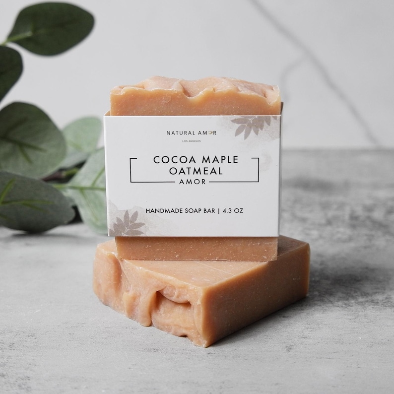 May include: A bar of handmade soap with a white label that reads "Natural Amor Los Angeles Cocoa Maple Oatmeal Amor Handmade Soap Bar | 4.3 oz".