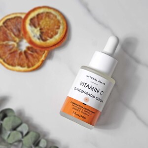 May include: A white and clear glass bottle of Vitamin C Concentrated Serum with a white dropper. The bottle has orange and white labels. Two dried orange slices are in the background. The bottle contains 1 fl oz or 30ml.