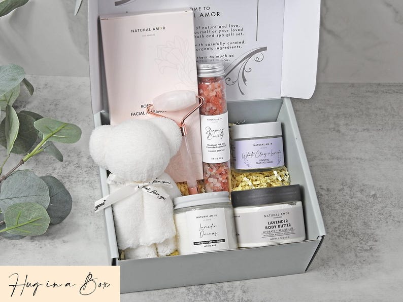 Puede incluir: Una caja de regalo que contiene un oso de peluche blanco, un rodillo facial rosa, un tubo de sales de ba&ntilde;o rosas, un tarro de mascarilla de arcilla blanca y lavanda, una vela de lavanda y un tarro de manteca corporal de lavanda.