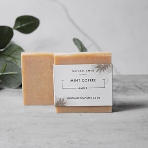 May include: A bar of handmade soap with a white label that reads "Natural Amor Los Angeles Mint Coffee Amor Handmade Soap Bar | 4.3 oz"