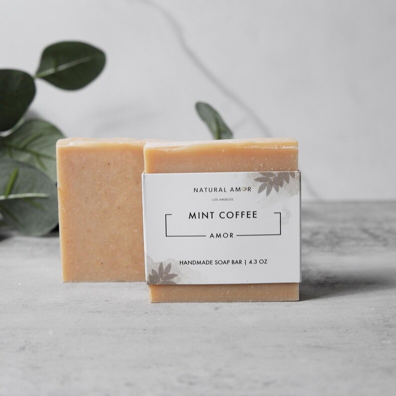 May include: A bar of handmade soap with a white label that reads "Natural Amor Los Angeles Mint Coffee Amor Handmade Soap Bar | 4.3 oz"