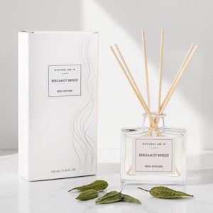 May include: A clear glass reed diffuser with wooden reeds and a white box. The box and the diffuser have labels that read "NATURAL AM" and "BERGAMOT BREEZE REED DIFFUSER". The box also indicates the volume is 100 ml / 3.34 fl oz.