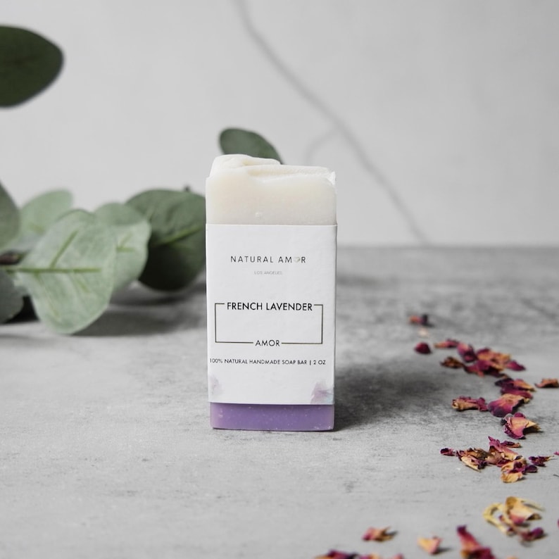 May include: A white bar of soap with a purple label that reads "NATURAL AMOR" and "FRENCH LAVENDER" with the text "AMOR" underneath. The soap bar is 100% natural handmade soap bar and is 1 oz.
