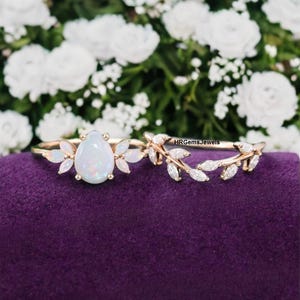 May include: A delicate opal engagement ring with a pear-shaped centre stone and a floral design. The ring is set in rose gold and features a matching wedding band with a leaf design.