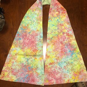 May include: A light green fabric scarf with a colorful pattern of circles in shades of pink, blue, yellow, and green.
