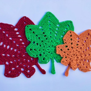 May include: Three crocheted leaf-shaped coasters in red, green, and orange.