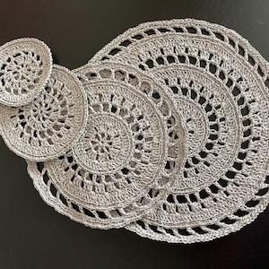 May include: Set of four crocheted gray doilies, with a larger doily in the center and three smaller doilies around it.
