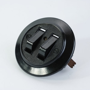 May include: A black bakelite double switch with two toggle switches. The switch is round and has a textured surface.