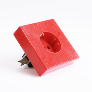 May include: A red plastic electrical outlet cover with a single round opening for a plug.