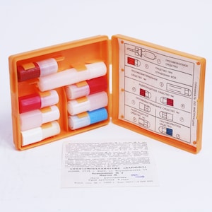 May include: An orange plastic first aid kit with a variety of small vials and a printed instruction sheet. The vials are labeled with numbers and colors. The instruction sheet has text in Russian.